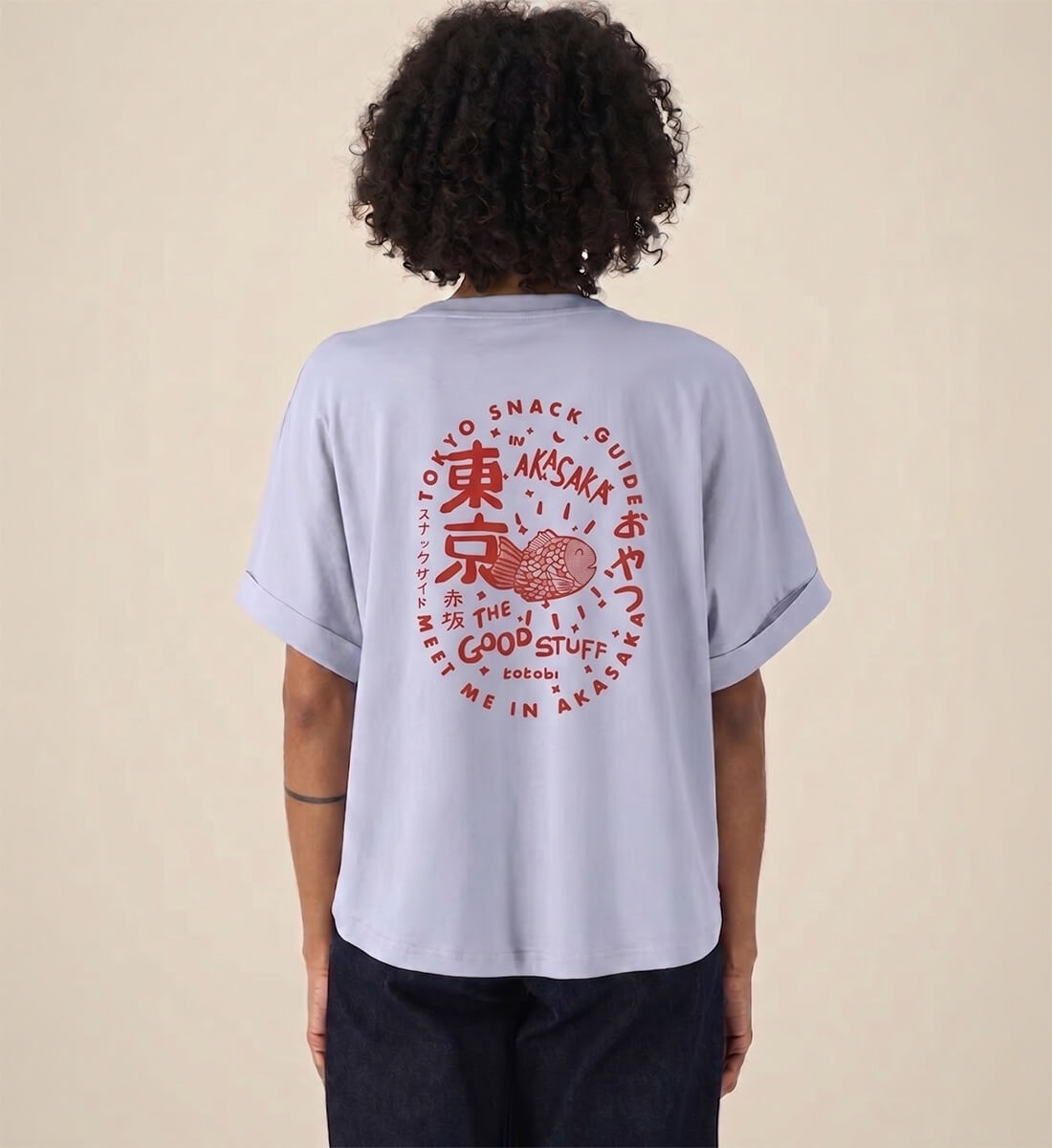 Rückenansicht eines hellblauen Damen T-Shirts. Großer, roter, kreisförmiger Backprint im Vintage-Stil mit der Aufschrift Tokyo Snack Guide Akasaka und der handgezeichneten Illustration eines japanischen Taiyaki-Gebäcks.