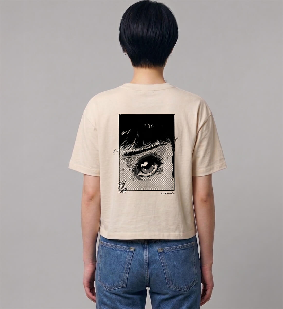 Rückenansicht einer Frau in blauer Jeans, die ein cremefarbenes, kurz geschnittenes Boxy T-Shirt trägt. Markanter schwarzer Backprint mit einem Retro 80er Jahre Manga-Auge im Panel-Stil.